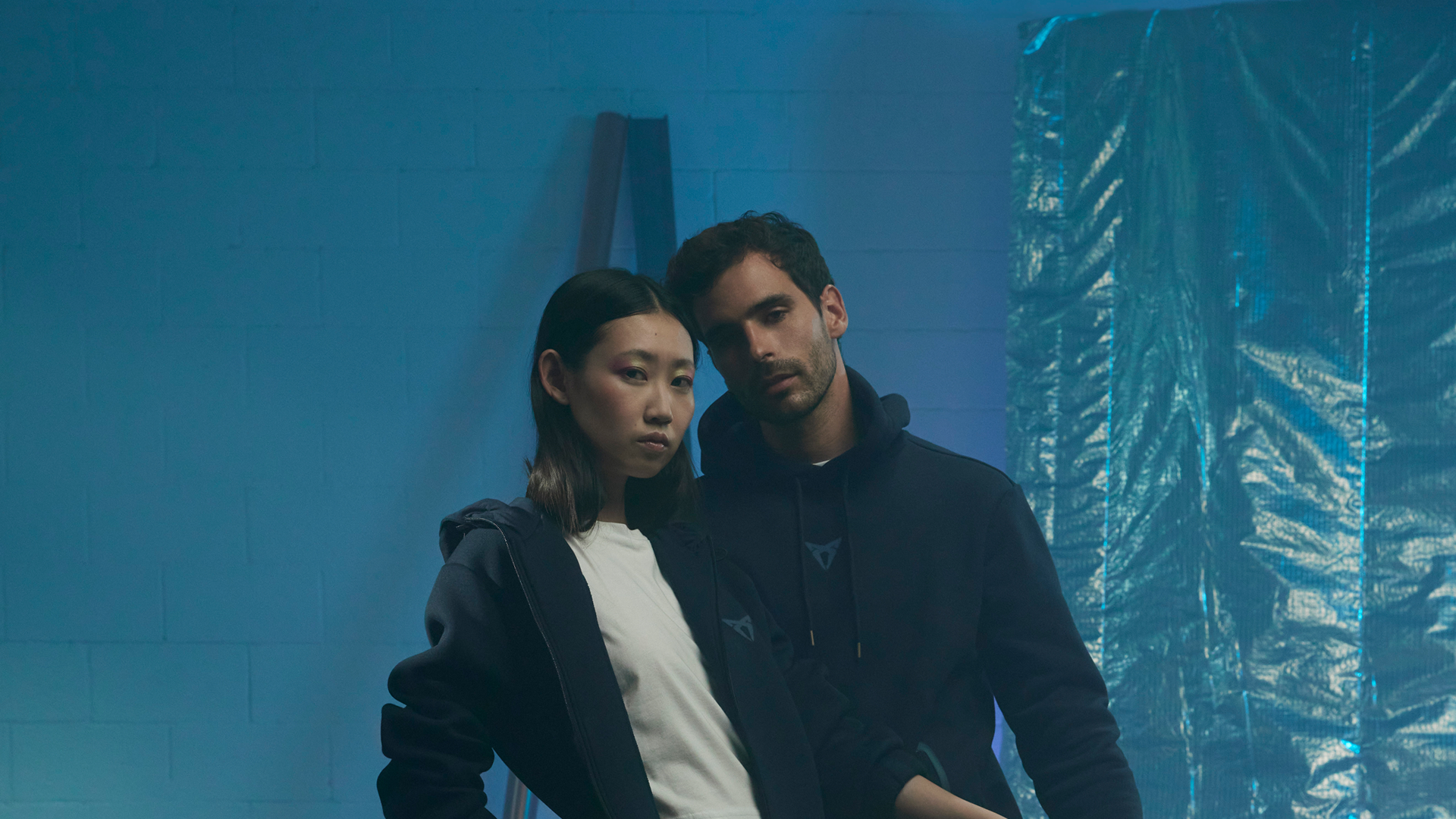 Zwei Personen in CUPRA Collection Kleidung, Hoodie in Dunkelblau mit CUPRA Logo